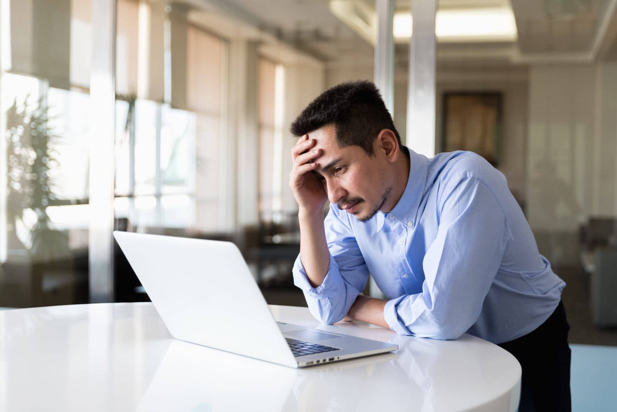 A young businessman using laptop standing working with strain in